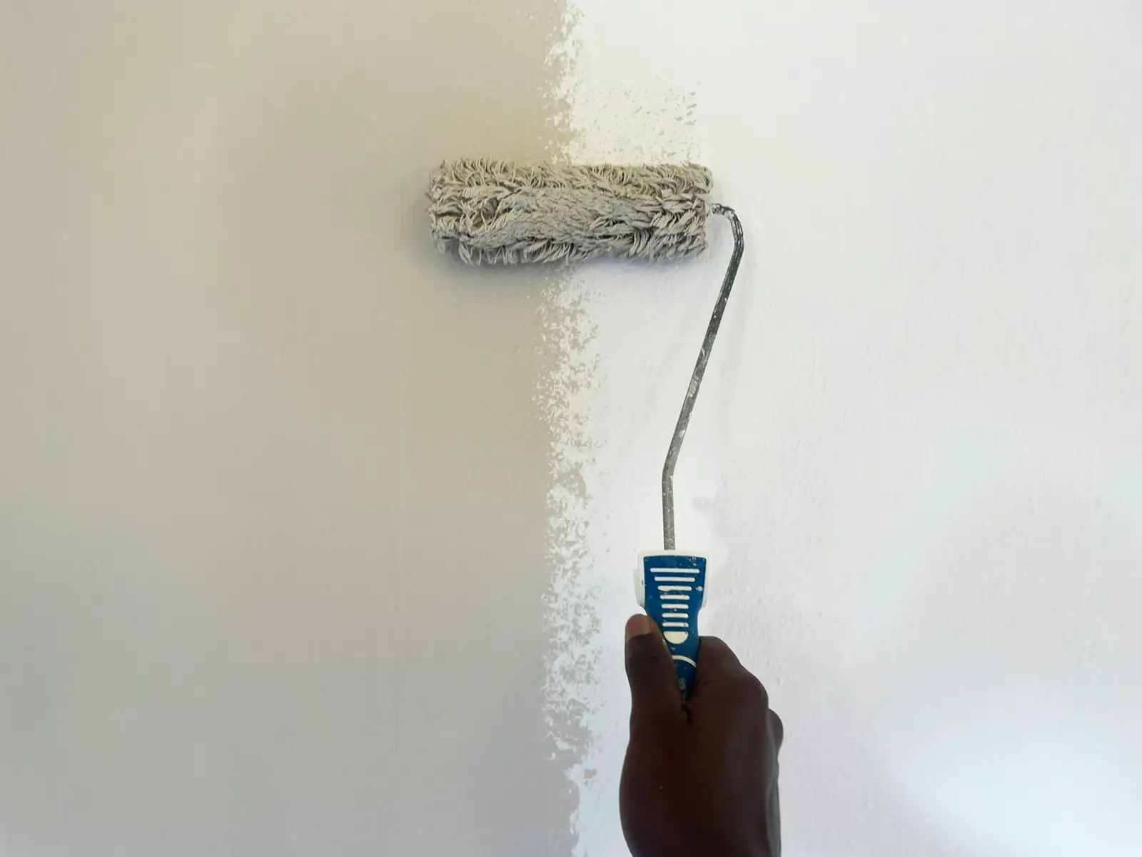 Eine frisch gestrichene weiße Wand mit einer Farbrolle mitten im Strich