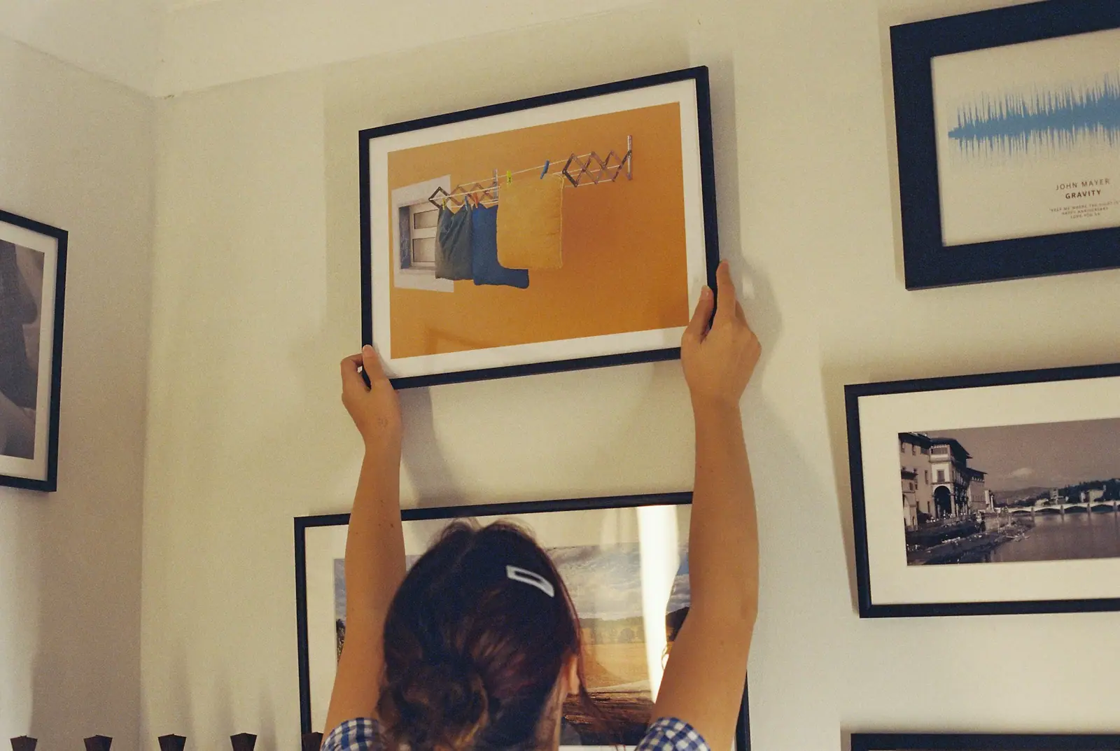 Eine Person hängt einen gerahmten Druck an eine Wand voller anderer gerahmter Bilder