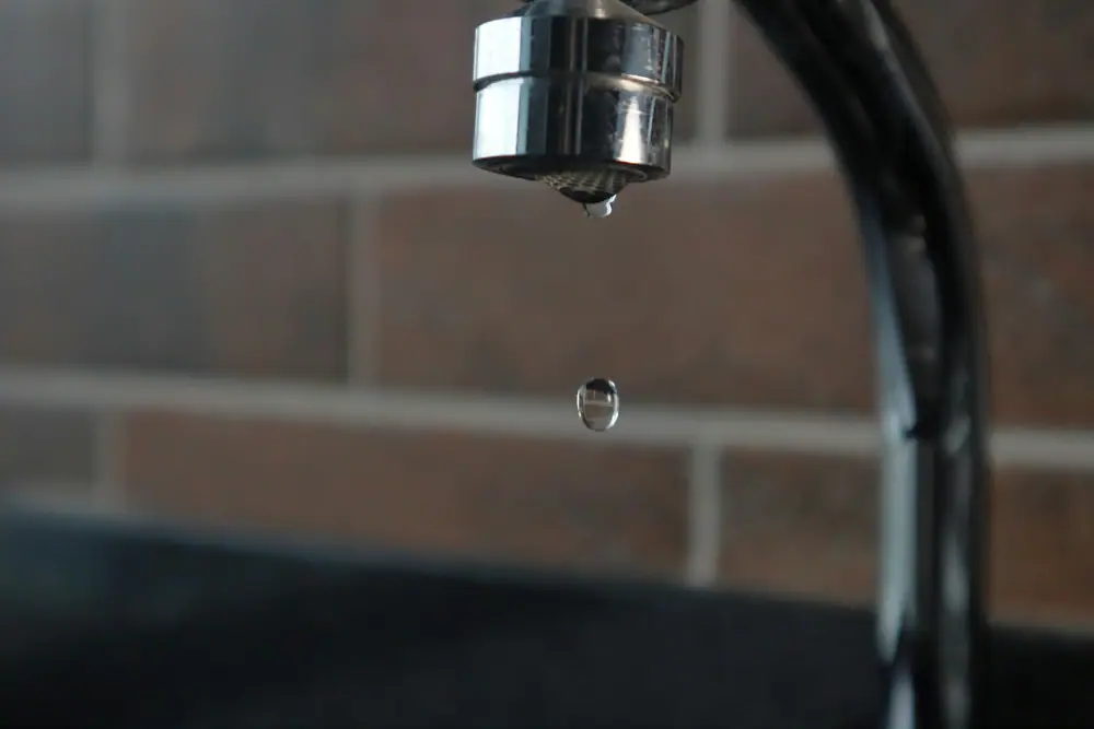 Ein Wassertropfen hängt am Auslauf eines verchromten Wasserhahns