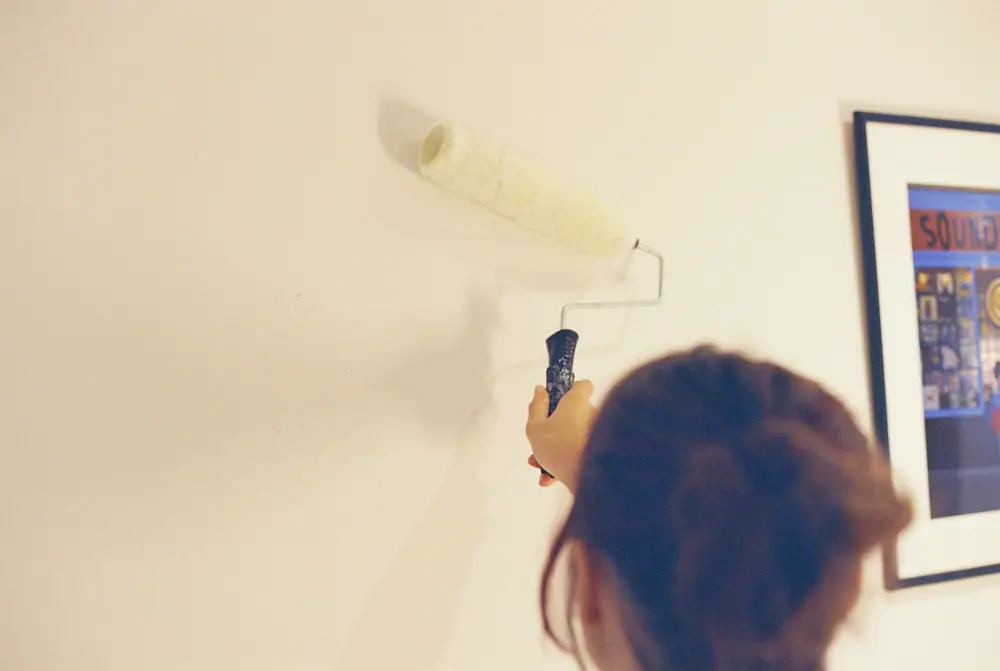 Eine Person rollt neben einem gerahmten Bild helle Farbe auf die Wand